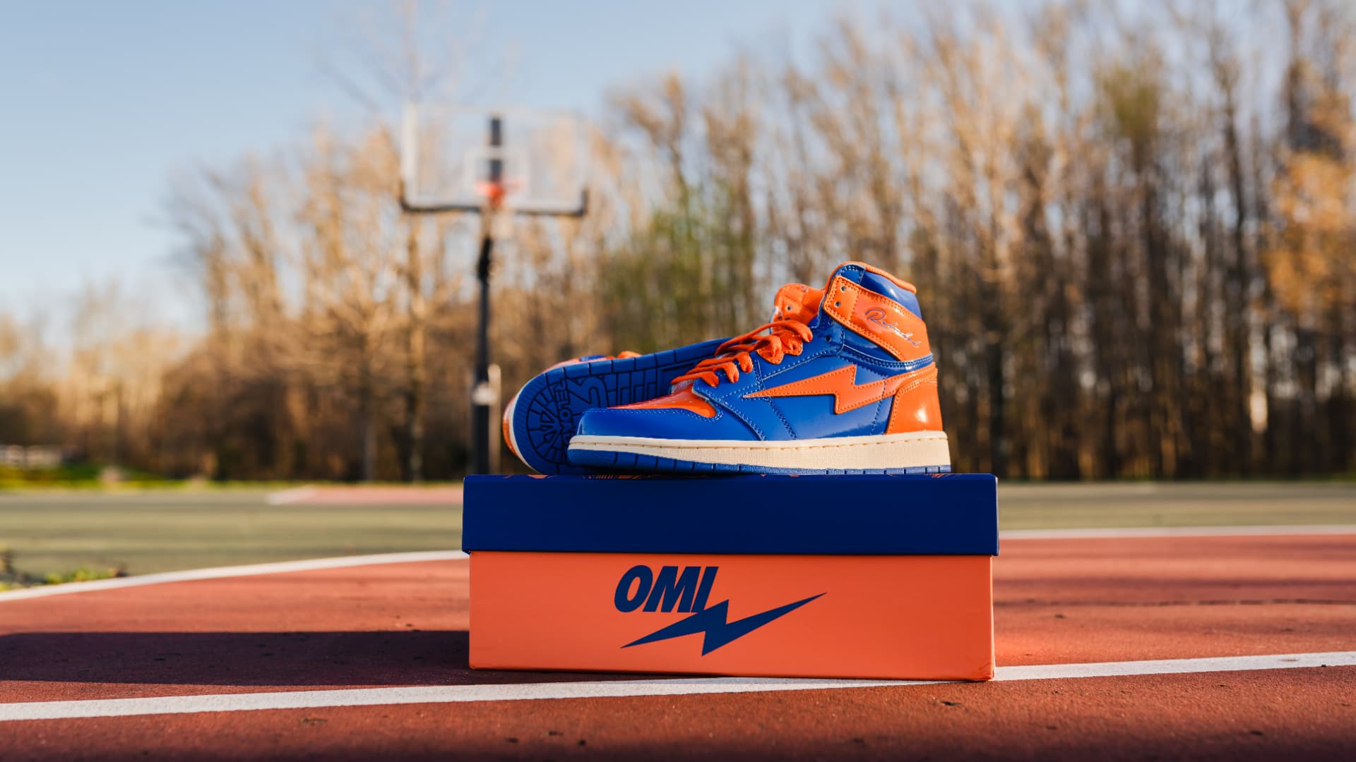 Blue and orange high-top sneaker displayed on its box on an outdoor court