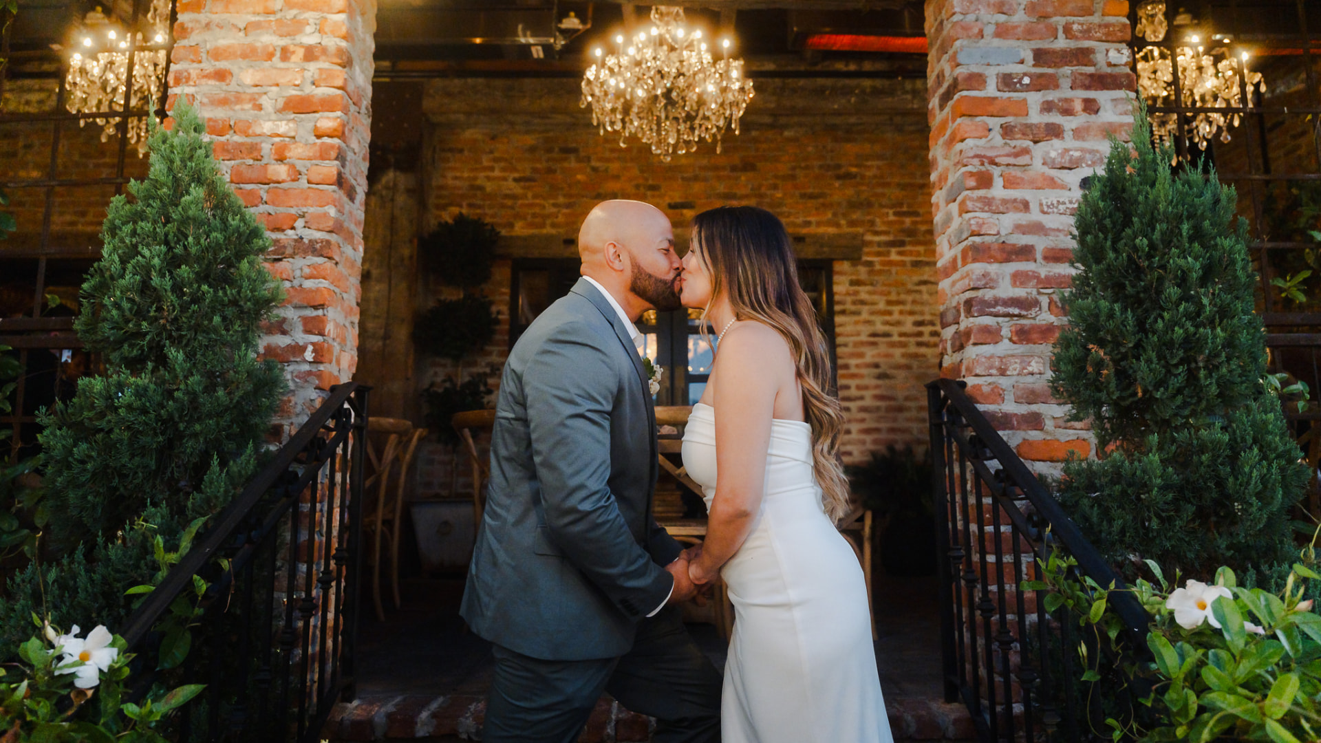 Bride and groom kissing under chandeliers at a brick wedding venue